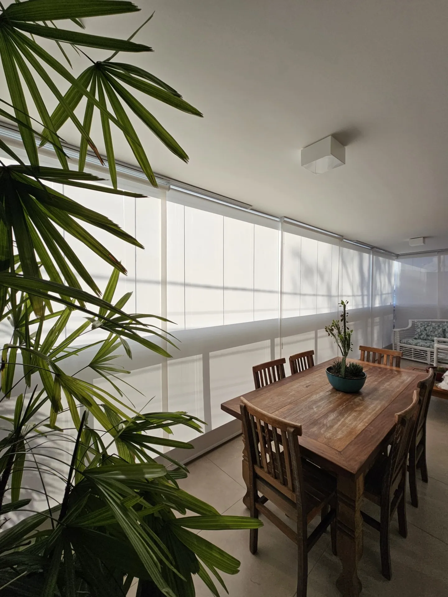 Persiana rolô branca em varanda com mesa de madeira e plantas